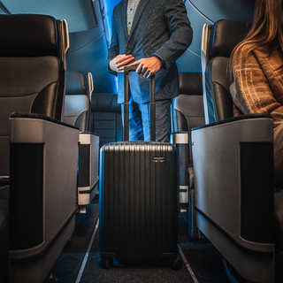 Traveler rolling a black NOMATIC Method Carry-On through the aisle of an airplane cabin.