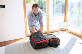 Man packing clothing into a black travel bag on a bed