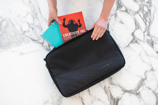 Hands placing a book into a black NOMATIC laptop sleeve