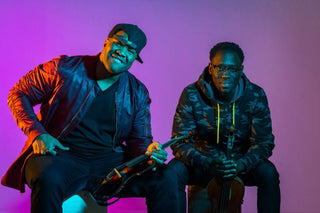 Two musicians holding violins against a purple background