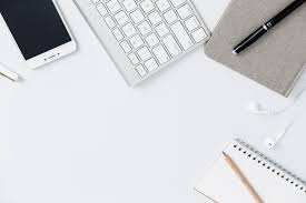 Minimal white desk with keyboard, notebook, phone, and pen