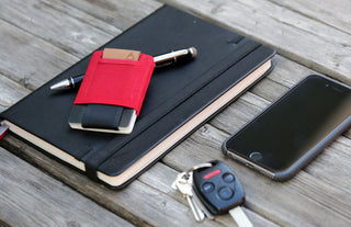 Red minimalist wallet with cards beside a notebook, phone, and keys