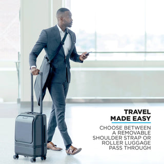 NOMATIC Garment Bag in Black, worn over the shoulder alongside rolling luggage
