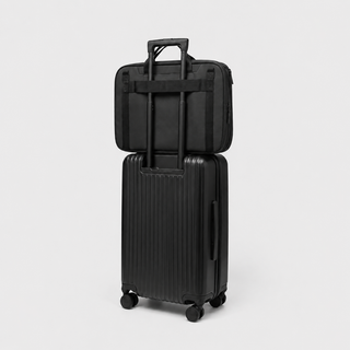 A black hard-shell rolling suitcase with an extended telescoping handle, stacked underneath a matching black soft-sided bag, photographed on a clean light gray studio background.