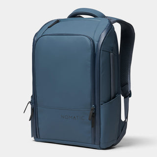 A slate blue Nomatic backpack shown from a three-quarter angle on a light gray background.