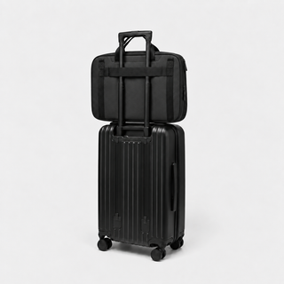 A black hard-shell rolling suitcase with an extended telescoping handle, stacked underneath a matching black soft-sided bag, photographed on a clean light gray studio background.