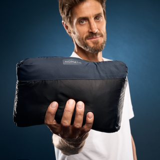 Man holding the NOMATIC Outset Jacket packed into its compact built-in storage pouch.