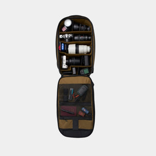 An open camera gear organizer bag shown from above on a white background, filled with lenses, accessories, cards, and small items in both compartments.