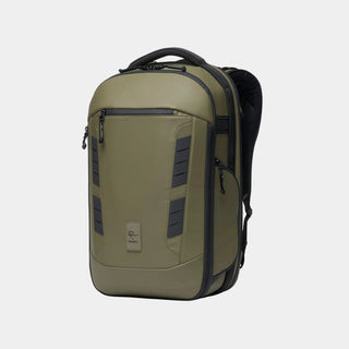 An olive green backpack with black accents, including zippers, trim, and side panels, shown on a clean white background. A small rectangular brand patch is visible on the lower front.