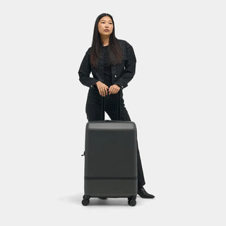 NOMATIC Check-In Classic in deep olive, lifestyle photo of a woman standing beside the bag