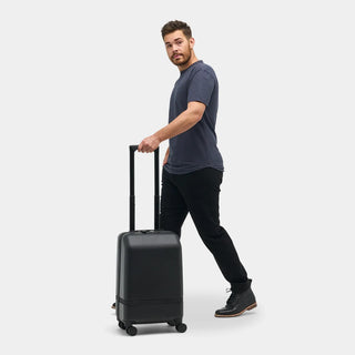 NOMATIC Carry-On Classic in black, lifestyle photo of a man walking with the bag rolling behind him