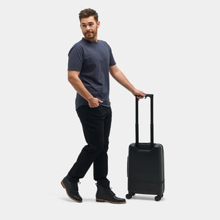 NOMATIC Carry-On Classic in black, close-up lifestyle photo of a man's hand on the extended pull handle while walking