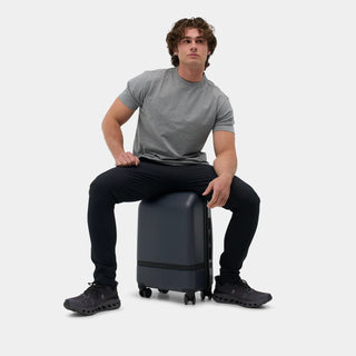 NOMATIC Carry-On Classic in navy, lifestyle photo of a man sitting on the bag