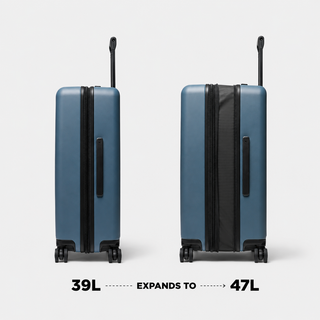 Two blue hard-shell spinner suitcases shown side by side on a light gray background, with text below reading '39L EXPANDS TO 47L'. The suitcase on the right shows the interior expansion flap.