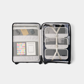An open black hard-shell suitcase shown from above, packed with travel organization accessories including mesh pockets, clear organizer pouches, straps, and small toiletry items on a light gray background.
