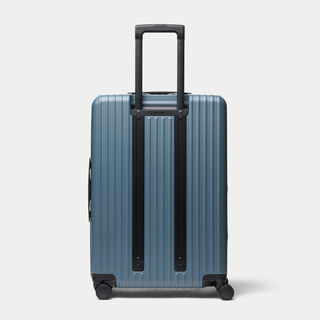 A blue ribbed hard-shell suitcase with an extended black telescoping handle and four spinner wheels, shown against a light gray studio background.
