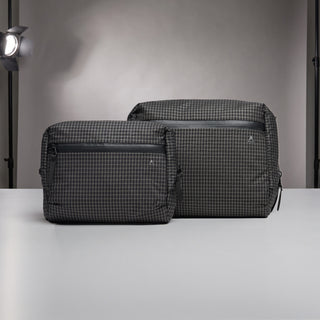 Two dark gray and black checkered travel or utility bags with black zippers, displayed on a light gray surface against a gray studio background.