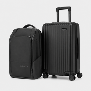 A black Nomatic backpack and matching black hard-shell spinner suitcase with telescoping handle, shown on a clean light gray studio background.